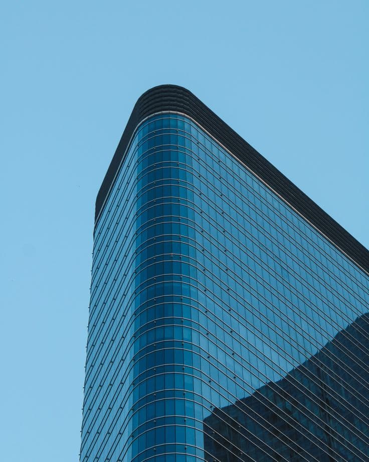 A glass office tower rising into a clear blue sky
